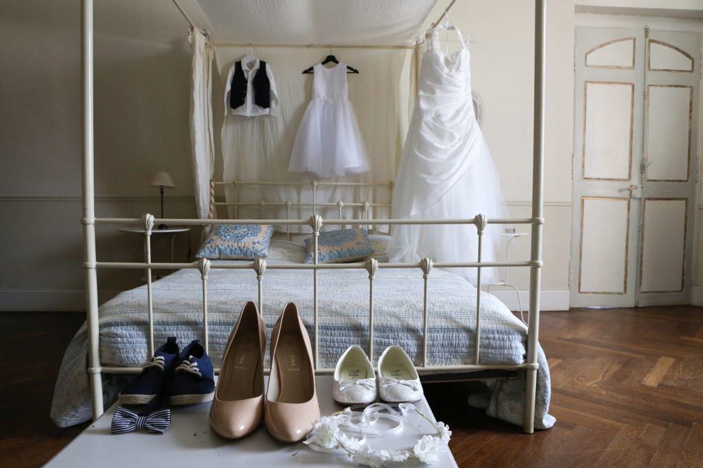 Robe de mariée et chaussures suspendues au baldaquin de la chambre du château de Riveneuve à louer pour des mariages