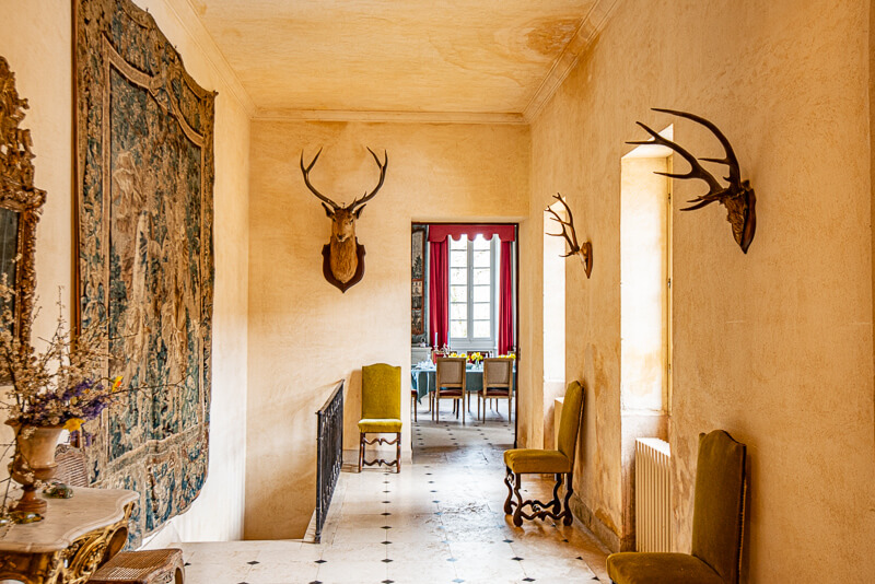Un couloir dans le château de Garraube accommodé d'une tapisserie, de bois de cerfs et de fauteils