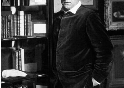 Portrait photo noir et blanc de Sacha Guitry devant une bibliothèque