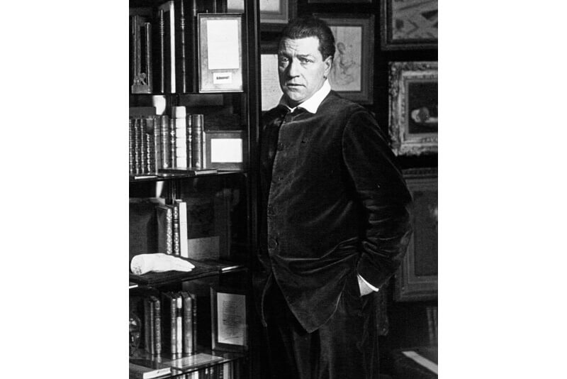 Portrait photo noir et blanc de Sacha Guitry devant une bibliothèque