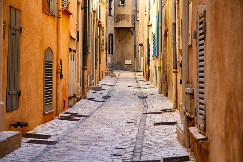 A paved and narrow road surounded by yellow building in Saint-Tropez