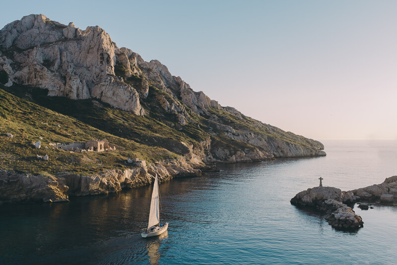 A sailing boat in a canal along the wild coast of Marseille at sunset.