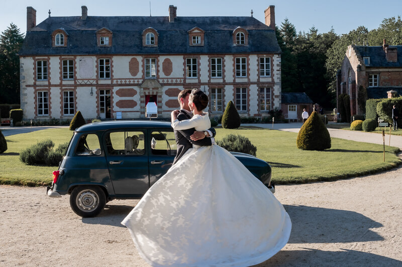 Les mariés s'embrassent devant une Renault 4L avec le château en fond